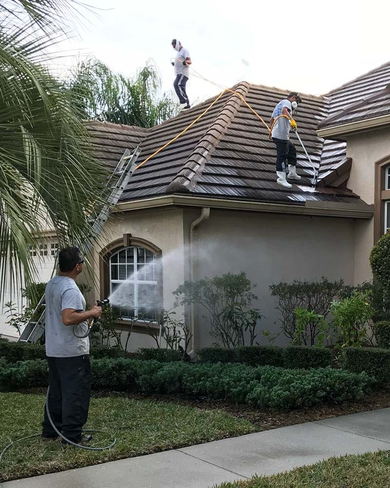 Crew pressure washing a tile roof and house exterior