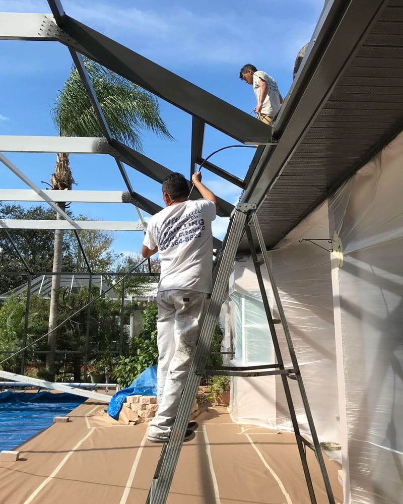 Two painters painting a pool cage frame